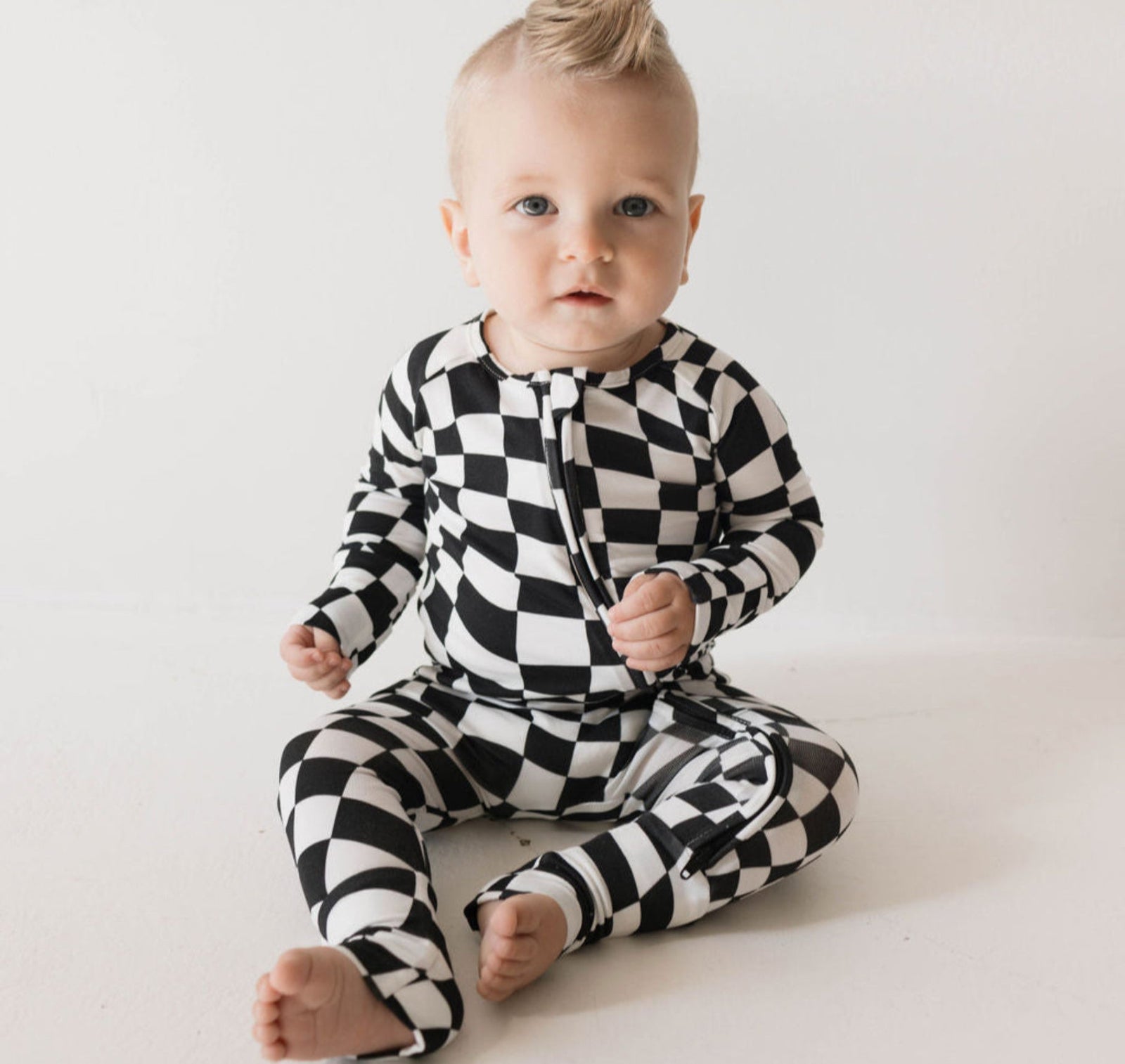 Baby wearing a black and white checkered outfit on a plain background