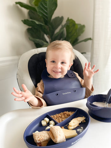 Baby wearing silicone bib with food catcher pocket. 