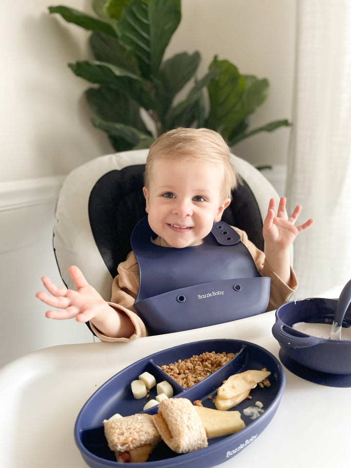 Baby wearing silicone bib with food catcher pocket. 