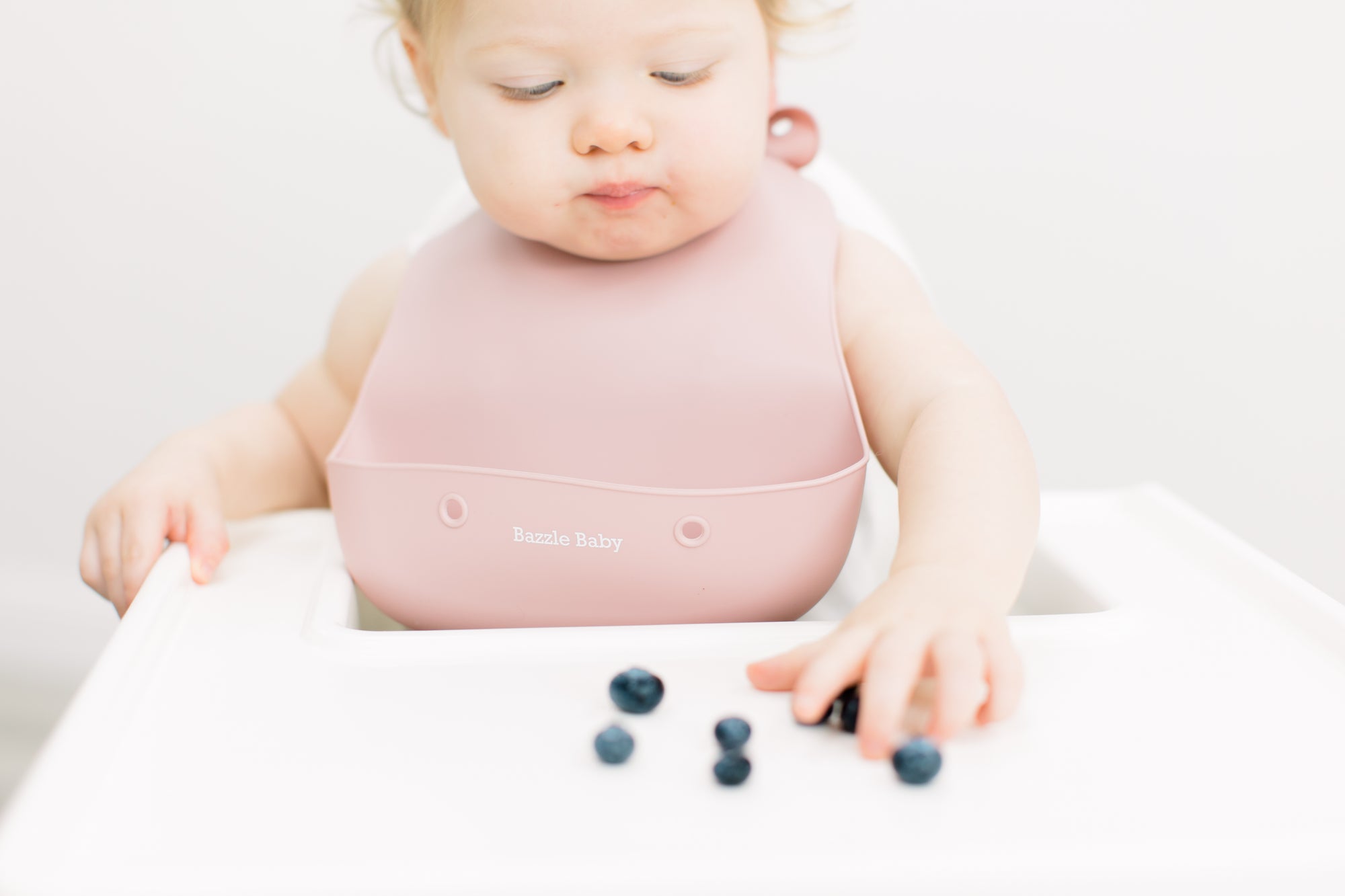 Baby wearing silicone bib with food catcher pocket in pink.