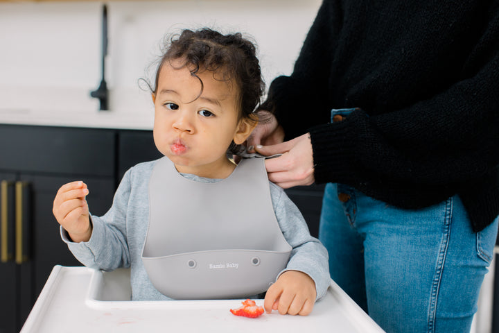 Baby wearing silicone bib with food catcher pocket in grey.