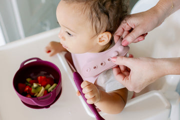 Baby wearing silicone bib with food catcher pocket. 