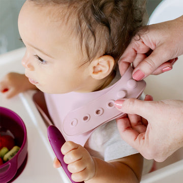 Baby wearing silicone bib with food catcher pocket. 