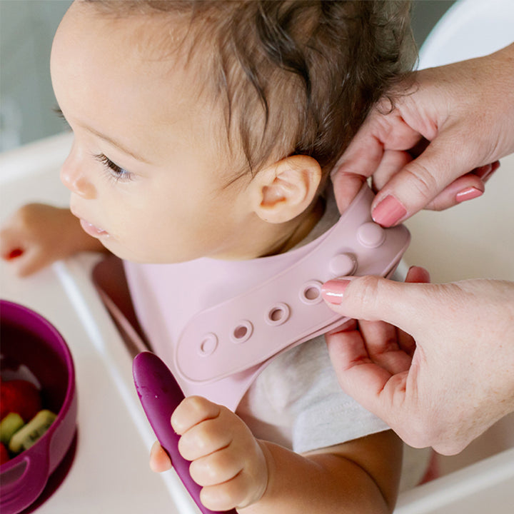 Baby wearing silicone bib with food catcher pocket. 