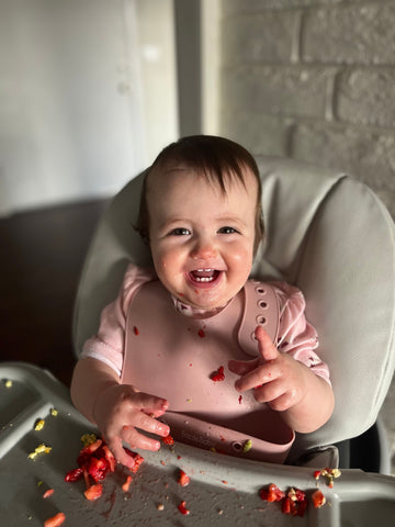 Baby wearing silicone bib with food catcher pocket. 