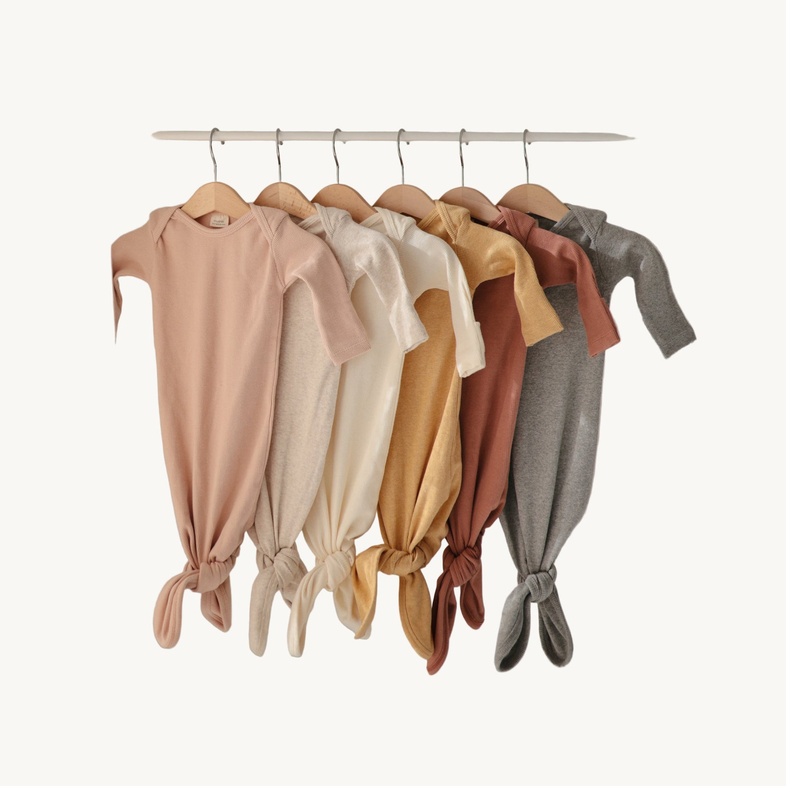 Row of baby onesies in various colors hanging on a rack against a neutral background