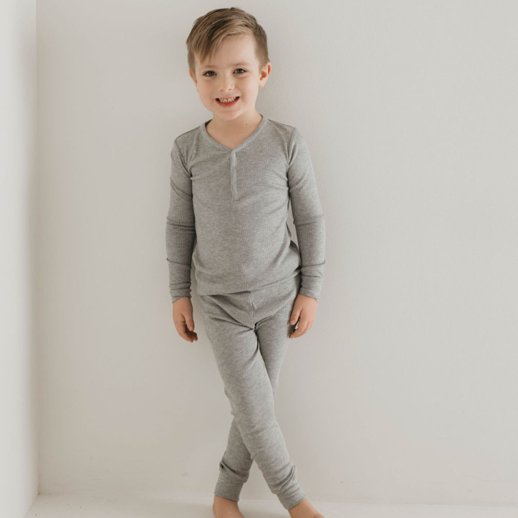 Young boy wearing gray pajamas standing against a plain white background