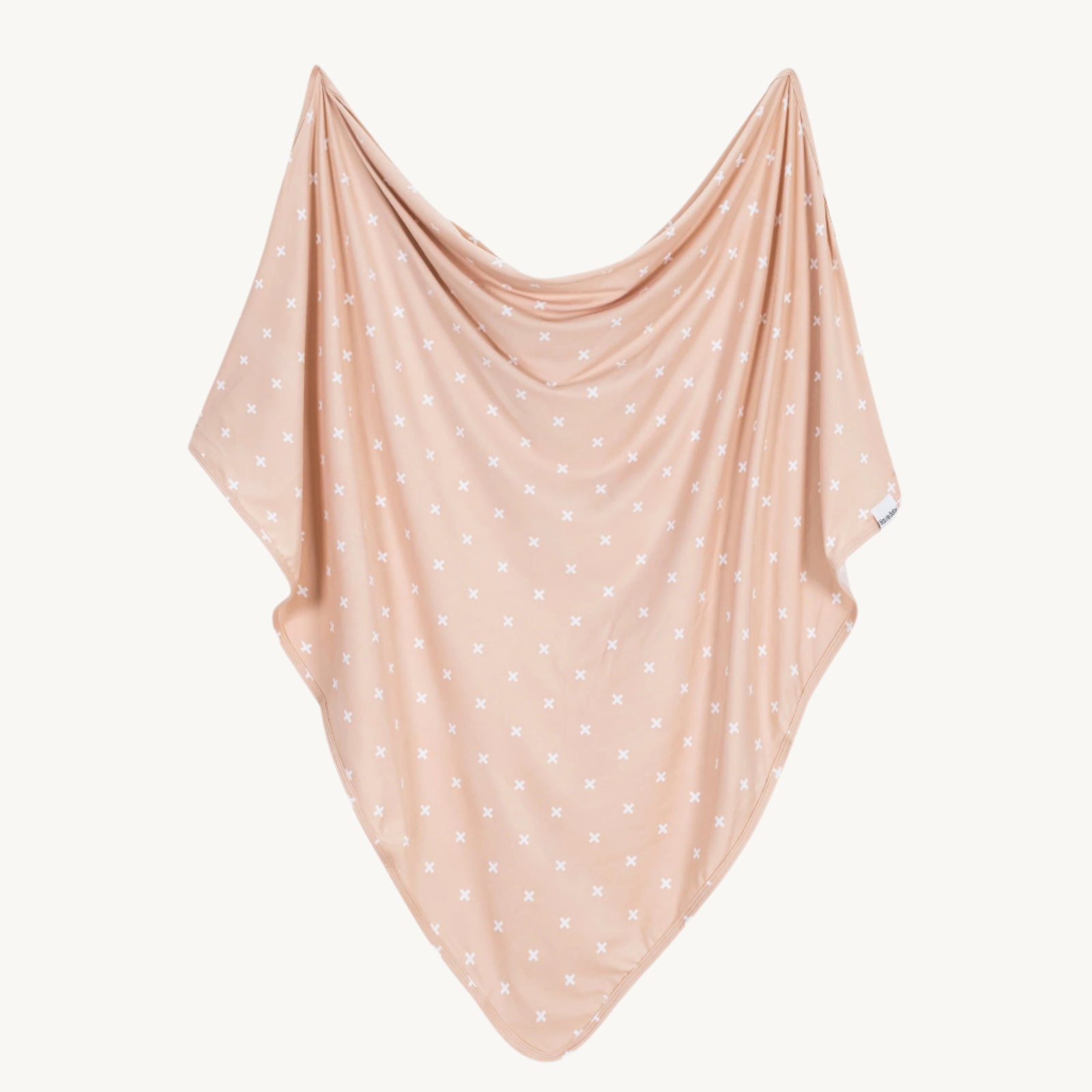 Beige polka dot fabric swaddle blanket draped over a white background