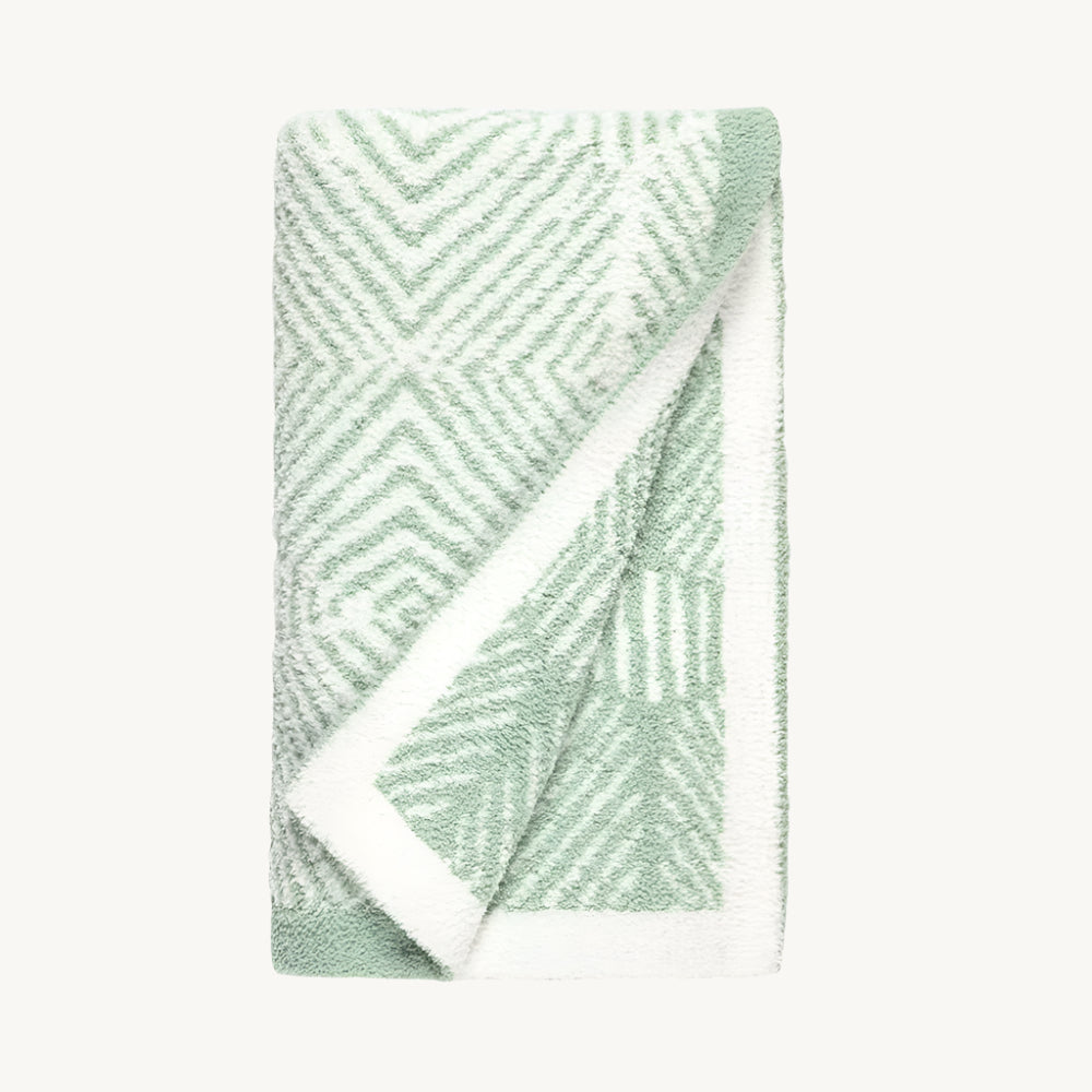 A sage green blanket on a gray and white geometric animal patterned blanket.