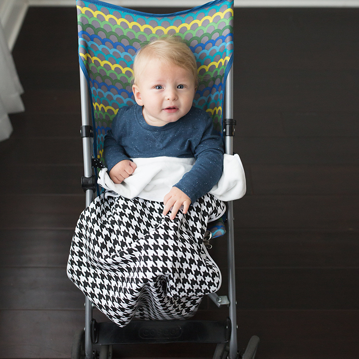Black and white houndstooth Bazzlebaby GoBlanket. Features clips on the sides of the blanket to ensure it stays put on the car seat, stroller or clothing. Cotton front and fleece back.