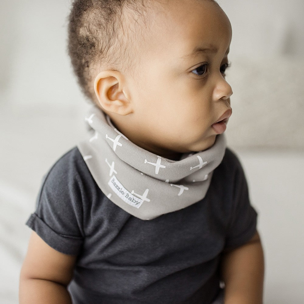Baby wearing infinity scarf drool bib in grey with white airplanes.