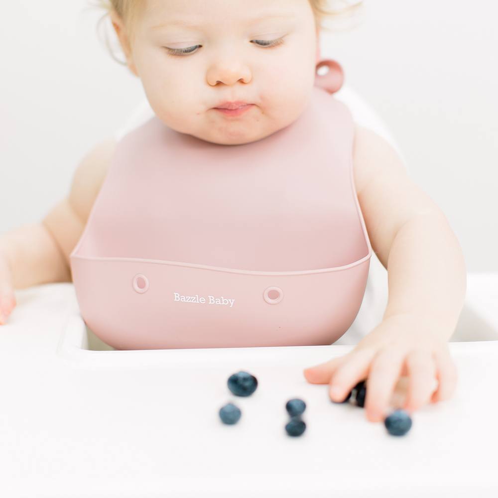 Baby wearing silicone bib with food catcher pocket. 