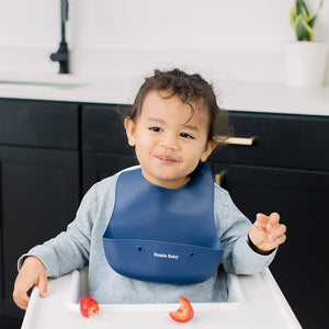 Baby wearing silicone bib with food catcher pocket. 