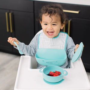 Baby wearing silicone bib with food catcher pocket. 