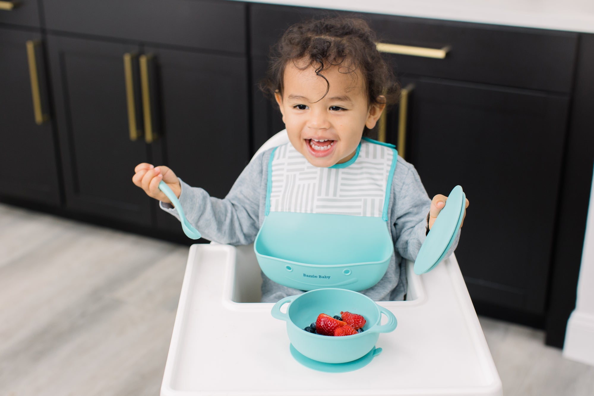 Baby wearing silicone feeding bib and using silicone bowl and spoon in Mint color. 