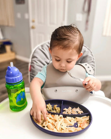 Baby wearing silicone bib with food catcher pocket. 
