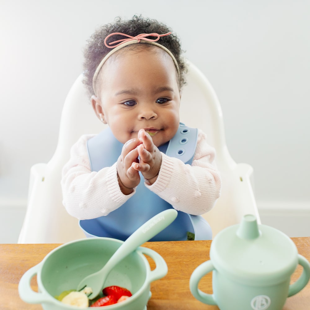 Baby wearing silicone bib with food catcher pocket. 