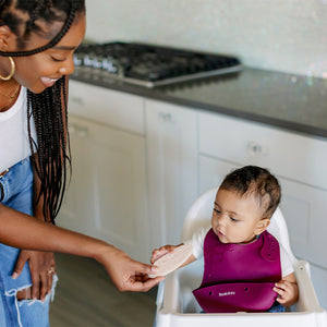 Baby wearing silicone bib with food catcher pocket. 